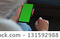 young woman sitting in a chair with smartphone with green screen 131592988