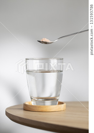 A spoon of Himalayan salt is being added to a glass of drinking water. A spoon of Himalayan salt is being added to a glass of drinking water. 131593786