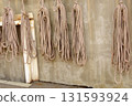 Bundles of various types of rope hang from the wall of a seaside warehouse. 131593924