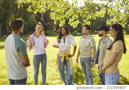 Company of happy young friends talking with each other standing in a circle in summer park. 131595697