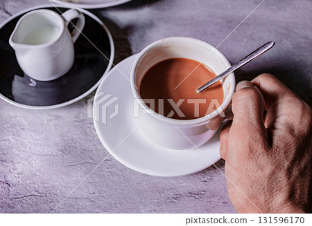 A hand holds a cup of coffee with milk A hand holds a cup of coffee with milk 131596170