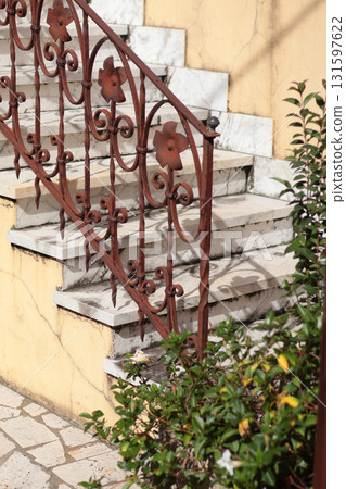 Old rusty wrought iron railings and marble steps at entrance to Italian house. Outdoor design and sunlight. Architectural contrast between wrought iron and marble. 131597622