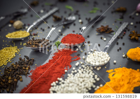 Collection of spices are spread out on a table. The spices include cumin, paprika, and turmeric 131598819