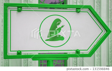 A sign indicating the place of prayer and depicting a Muslim woman, against the backdrop of a mosque wall A sign indicating the place of prayer and depicting a Muslim woman, against the backdrop of a mosque wall 131598846