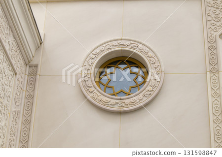A round window with floral ornamentation and a carved frame on the white marble wall of the mosque A round window with floral ornamentation and a carved frame on the white marble wall of the mosque 131598847