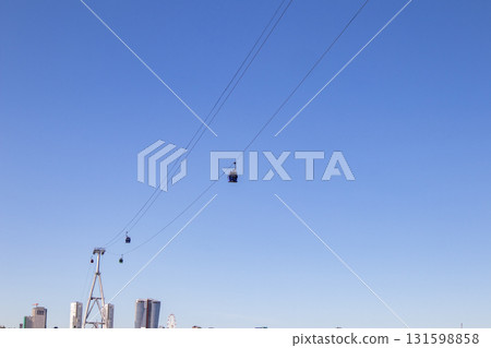 The cable car cabins move along a steel cable against the backdrop of a blue sky. The cable car cabins move along a steel cable against the backdrop of a blue sky. 131598858
