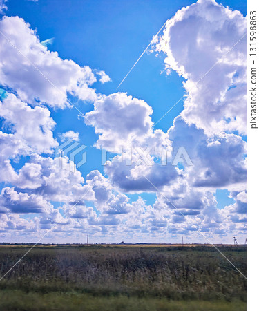 Cumulus clouds and airplane contrail over field under blue sky, horizontal frame Cumulus clouds and airplane contrail over field under blue sky, horizontal frame 131598863