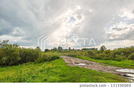 Muddy rural road with puddles and a fork under an overcast sky, countryside landscape Muddy rural road with puddles and a fork under an overcast sky, countryside landscape 131598869