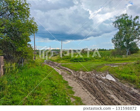 Country dirt road and power lines across green meadows under a cloudy sky Country dirt road and power lines across green meadows under a cloudy sky 131598872