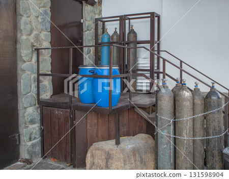 Gas cylinders and blue plastic drums at warehouse ramp, chained for storage safety, industry Gas cylinders and blue plastic drums at warehouse ramp, chained for storage safety, industry 131598904