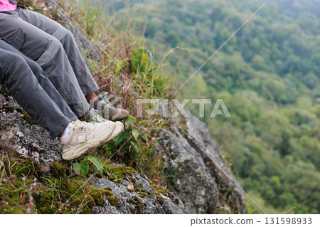 Close up of hiker resting on rocky cliff in hiking shoes, symbol of adventure, outdoor lifestyle, challenge, exploration, determination, nature journey and freedom in mountain travel. Close up of hiker resting on rocky cliff in hiking shoes, symbol of adventure, outdoor lifestyle, challenge, exploration, determination, nature journey and freedom in mountain travel. 131598933