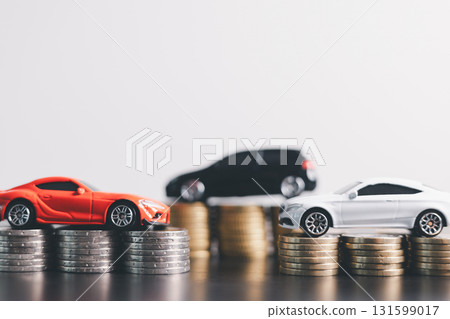 Three car models in red, black and white placed on stacks of money with scattered coins, representing auto loan, car finance, investment, insurance, leasing, savings concept. car finance, investment 131599017