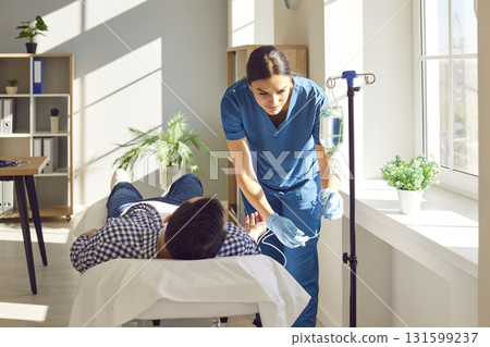 Young friendly nurse help male patient in receiving IV drip infusion and vitamin therapy in clinic Young friendly nurse help male patient in receiving IV drip infusion and vitamin therapy in clinic 131599237