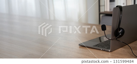 Customer support headset resting on laptop in modern office, daylight bokeh, symbolizing call center service, helpline communication, remote work, and tech assistance. 131599484