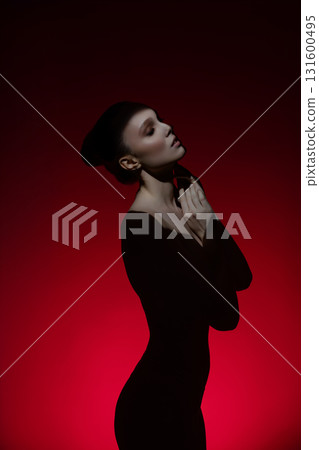 Captivating silhouette of a woman with elegant pose against a red backdrop 131600495