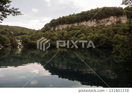 A rocky cliff is reflected in a clear mountain lake 131601338