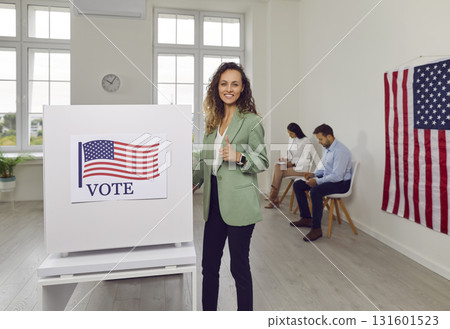 Voter woman looking at camera standing at vote center near voting booth on election day. 131601523