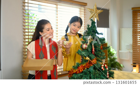 Mother and child decorating a Christmas tree together to celebrate the upcoming holiday season. Family celebration in winter holiday / New Year season 131601655