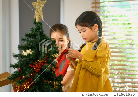 Mother and child decorating a Christmas tree together to celebrate the upcoming holiday season. Family celebration in winter holiday / New Year season Mother and child decorating a Christmas tree together to celebrate the upcoming holiday season. Family celebration in winter holiday / New Year season 131601659