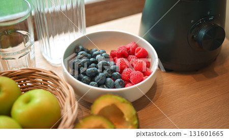 Healthy lifestyle setup in the kitchen. Fresh fruits apples, blueberries, raspberries, and avocado arranged beside a blender, prepared for making a homemade smoothie Healthy lifestyle setup in the kitchen. Fresh fruits apples, blueberries, raspberries, and avocado arranged beside a blender, prepared for making a homemade smoothie 131601665