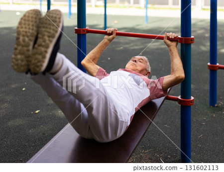 Old man doing leg raise exercise outdoors 131602113