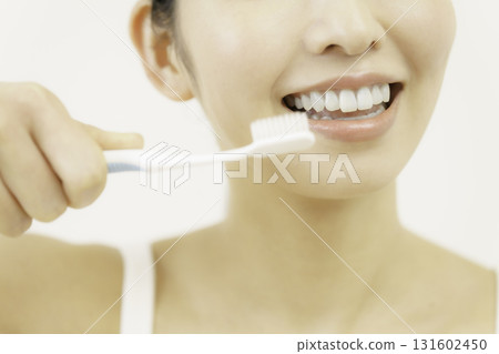 Close-up of the face under the eyes of a young woman brushing her teeth against a white background Close-up of the face under the eyes of a young woman brushing her teeth against a white background 131602450