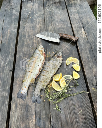 Fresh trout on a rustic wooden board with a knife. Natural light highlights the texture of the fish and wood.  131603106