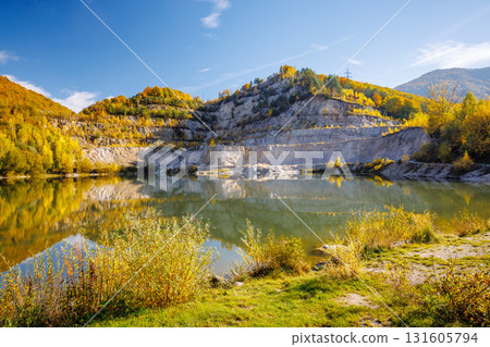 Autumn landscape with a lake by the hills covered with colorful trees. Flooded quarry near the village Sutovo in Slovakia, Europe. 131605794