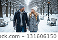 A couple holding hands walking in a snowy park with trees and benches on a winter day looking at each other 131606150