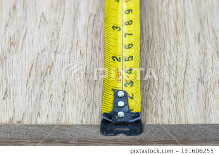 Measuring tape yellow metal wood closeup tool metric imperial inch scale snug focus measuring tape against wood board, precise craft mood, workshop vibe, carpentry detail, accuracy and build pride 131606255