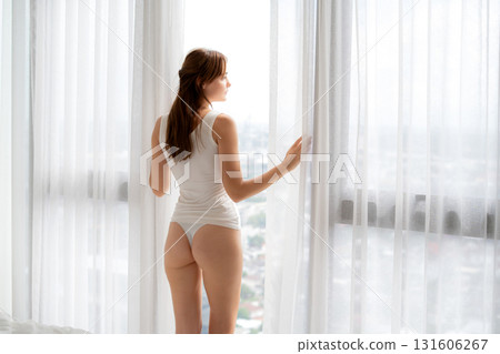 Young caucasian woman standing looking window in morning at home, relaxation after wake up. Young caucasian woman standing looking window in morning at home, relaxation after wake up. 131606267