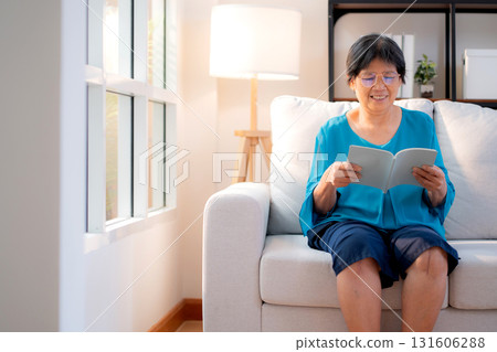 Asian senior woman reading a book sitting on sofa with relax in living room at home. 131606288