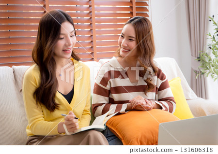 Two asian woman sitting on sofa using laptop computer video call and note taking together. Two asian woman sitting on sofa using laptop computer video call and note taking together. 131606318