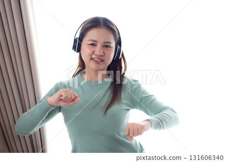 Happy young asian woman wearing headphones listening music while standing dancing with fun. Happy young asian woman wearing headphones listening music while standing dancing with fun. 131606340