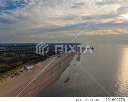 Aerial view of coastal city with long sandy beach, scattered structures, and pier showcasing contrast between urban skyline and serene shoreline under partly cloudy skies. Aerial view of coastal city with long sandy beach, scattered structures, and pier showcasing contrast between urban skyline and serene shoreline under partly cloudy skies. 131606770