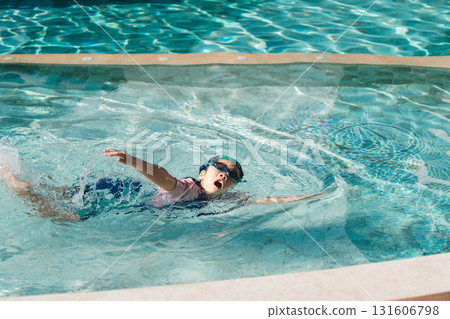 Child Playing Joyfully in Swimming Pool Water Wearing Goggles and Swimming Trunks in Bright Sunlight Splashing Water with Excitement 131606798