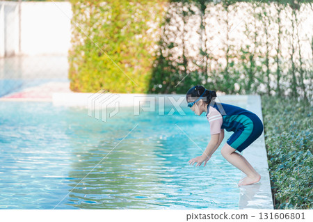 Young child preparing to dive into a refreshing pool water, wearing swim gear and goggles, sunny day with greenery in the background, summer fun at home Young child preparing to dive into a refreshing pool water, wearing swim gear and goggles, sunny day with greenery in the background, summer fun at home 131606801