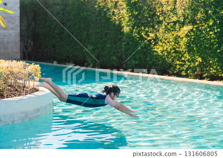 Child Diving Into Crystal Clear Swimming Pool Water in a Bright Sunny Day Surrounded by Lush Greenery and Relaxing Outdoor Ambiance Child Diving Into Crystal Clear Swimming Pool Water in a Bright Sunny Day Surrounded by Lush Greenery and Relaxing Outdoor Ambiance 131606805