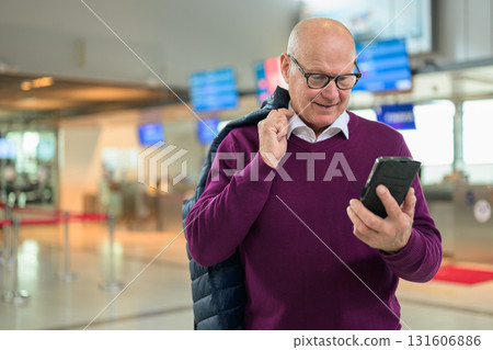 Portrait of happy senior man using mobile phone while standing in airport 131606886
