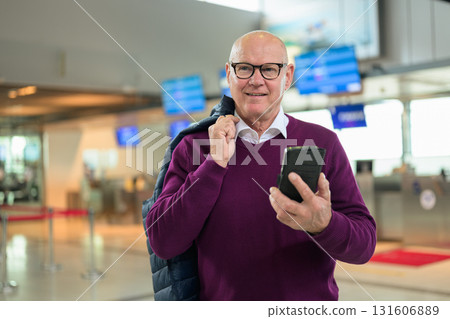 Portrait of happy senior man using mobile phone while standing in airport Portrait of happy senior man using mobile phone while standing in airport 131606889