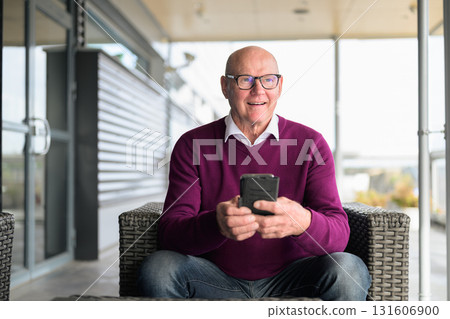 Portrait of happy senior man using mobile phone while sitting in armchair Portrait of happy senior man using mobile phone while sitting in armchair 131606900
