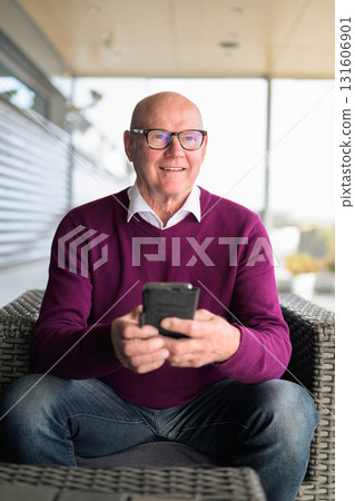 Portrait of happy senior man using mobile phone while sitting in armchair 131606901