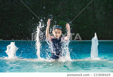 Happy child playing in swimming pool, splashing water with hands raised, enjoying summer day under bright sunlight with playful energy and joy 131606929