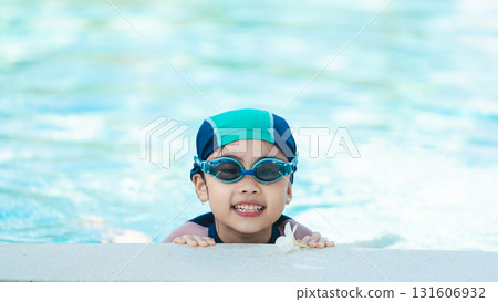 Happy child with swim goggles smiling in water while holding onto pool edge, enjoying a playful summer day in bright sunlight and clear water 131606932