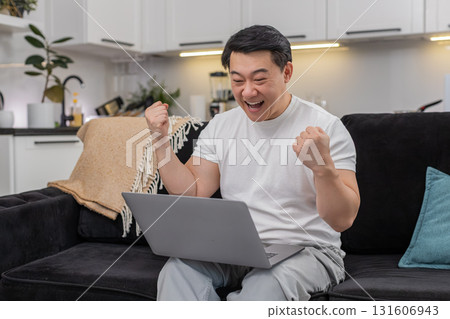 Asian man celebrates work project success on laptop smiles makes victory sign and sends final report 131606943