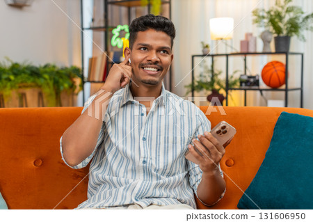 Indian man with earphones answers smartphone call speaks calm listens with focus on audio voice chat Indian man with earphones answers smartphone call speaks calm listens with focus on audio voice chat 131606950