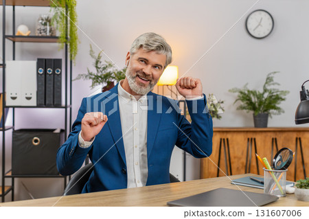 Middle-aged businessman dances on chair wearing earphones singing rock music after working on laptop Middle-aged businessman dances on chair wearing earphones singing rock music after working on laptop 131607006