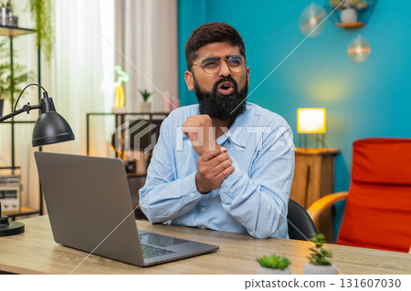 Indian man massaging painful wrist after long laptop work deep repetitive strain injury indoors Indian man massaging painful wrist after long laptop work deep repetitive strain injury indoors 131607030