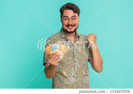 Man holding raising euro cash money in excitement smiling celebrating financial win or achievement Man holding raising euro cash money in excitement smiling celebrating financial win or achievement 131607056