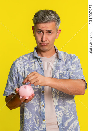 Man holding piggy bank dropping last coin sighing showing saving effort or poor money condition 131607071